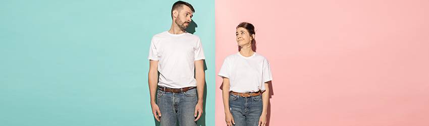 A man and a woman, both wearing white shirts, brown belts, and jeans, stand facing forward and look at each other sideways.