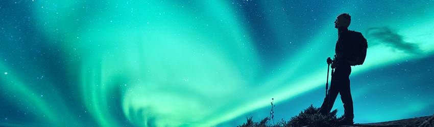 A backpacker's silhouette on a blue and green swirled sky.