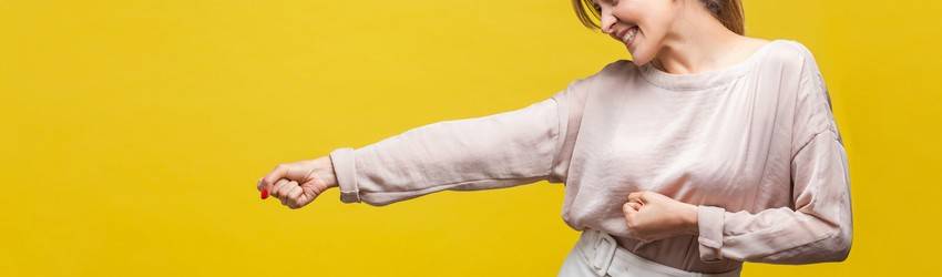 woman against yellow background punching the air with a smile