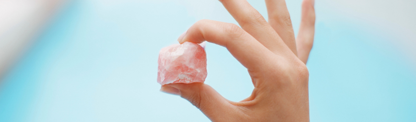 A person holding a rose quartz crystal in front of a pool.