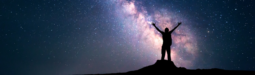 A silhouetted figure stands among the night sky and the constellations in the sky.